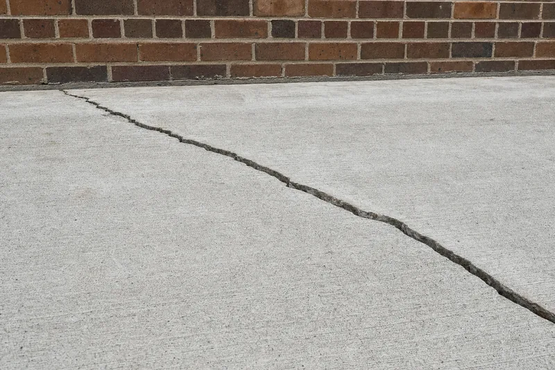 A concrete slab with a diagonal crack running across it toward the base of a brick wall — underpinning, Newcastle. Illustrative example.